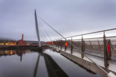 Editoryal Swansea, İngiltere - 16 Şubat 2019: Tawe Nehri üzerindeki Millennium köprüsünün sabahın erken saatlerinde sisli bir görünümü, Swansea'nin marina alanı etrafındaki yeni gelişmeyi gösteriyor.