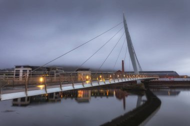 Editoryal Swansea, İngiltere - 16 Şubat 2019: Tawe Nehri üzerindeki Millennium köprüsünün sabahın erken saatlerinde sisli bir görünümü, Swansea'nin marina alanı etrafındaki yeni gelişmeyi gösteriyor.