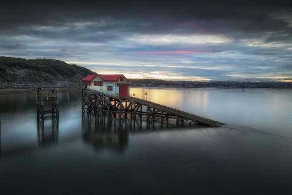 Mumbles Pier, Swansea Bay, Güney Galler, İngiltere'deki eski filika istasyonunda gün batımı ve sakin bir akşam gelgiti