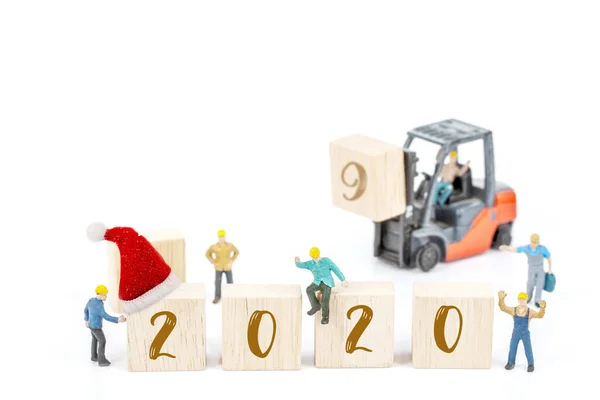 白い背景に木製のブロックに白い2020番号とフォークリフトマシンの前に立っているミニチュア労働者チームの建物 新年の2020コンセプトへの装飾 — ストック写真
