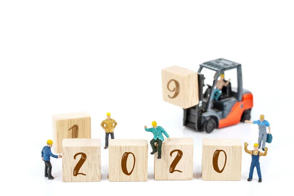 白い背景に木製のブロックに白い2020番号とフォークリフトマシンの前に立っているミニチュア労働者チームの建物 新年の2020コンセプトへの装飾 — ストック写真
