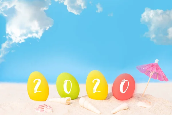 青い海の上の白い砂浜のカラフルな卵に2020テキスト 幸せな新年2020またはイースター休暇のコンセプト — ストック写真