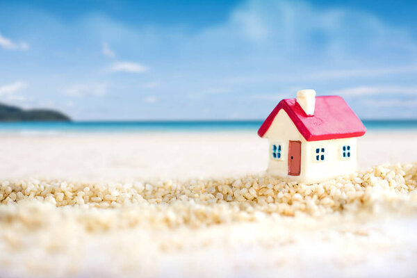 миниатюрный дом с красной крышей на песчаном пляже над размытым ясным небом в полдень.
. 