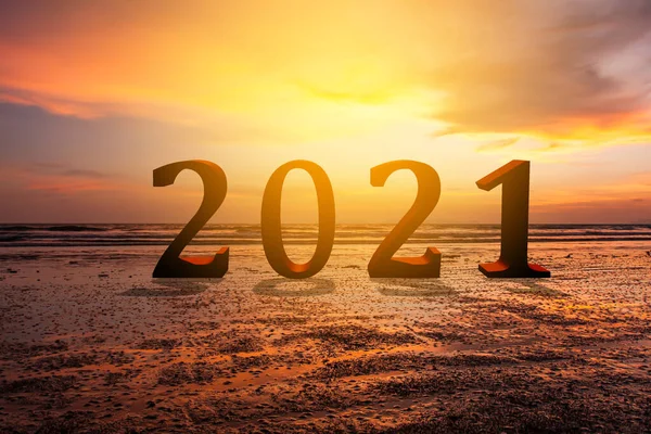 2021 text on sand beach over blurred sunset sky background for new year concept.