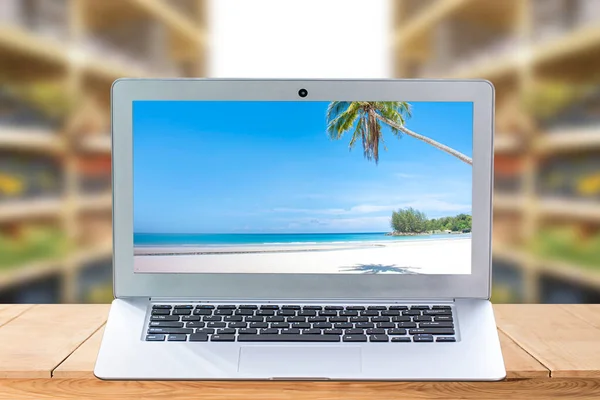 laptop or notebook with image beach  blue sea and clear sky on wooden mock up over blurred background for advertising poster at summer beach advertisement vacation.