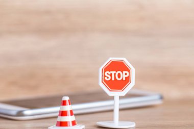 Ahşap zemindeki bulanık akıllı telefonun üzerinde trafik konisi olan dur işareti 