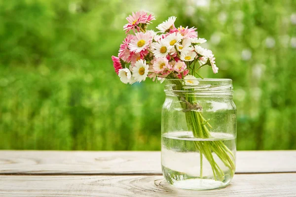 緑の背景に庭の木製のボードに夏にガラス瓶の花瓶にヒナギクの花の花束 ロイヤリティフリーのストック写真