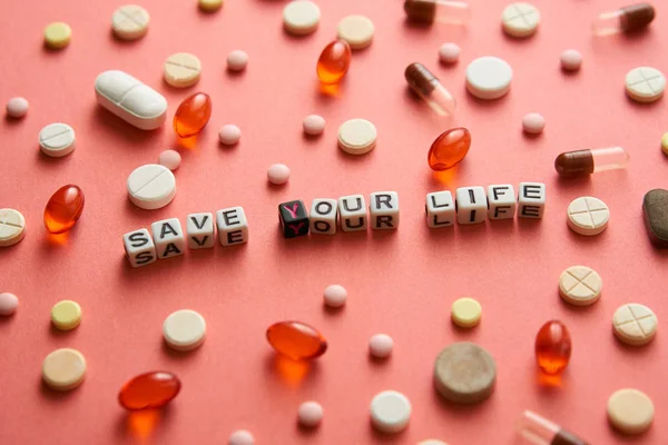 Multicolored title SAVE YOUR LIFE from white and black cubes on the table with tablets on coral background