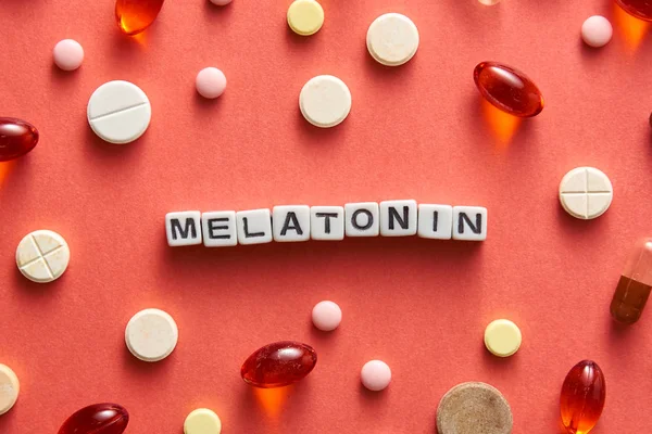 Black and white title MELATONIN from white cubes on the table with tablets on coral background