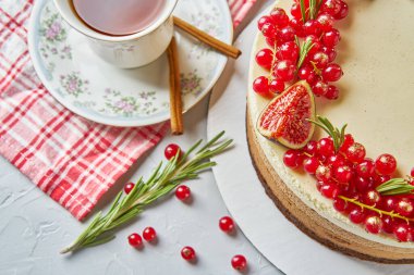 Yuvarlak ev yapımı kek kırmızı kuş üzümü, incir, tarçın ve biberiye masa örtüsü, Fincan ve tabak hafif bir arka plan beton masa ile dekore.