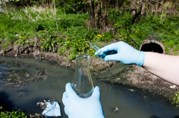 Su örneği için el eldiven bir ampul ve bir test tüpünde bir kanalizasyon boru, kirli su arka planı ile iade edin. Kirliliği ekoloji, çevre