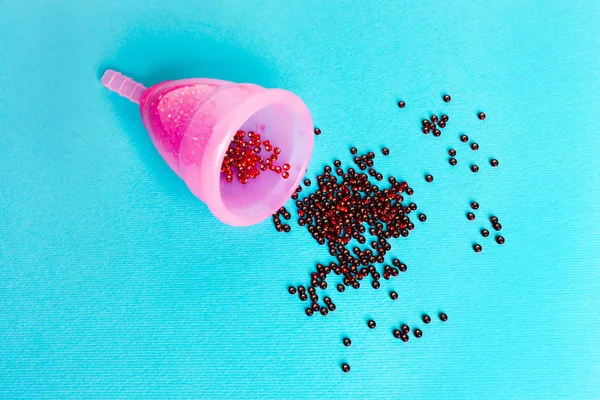 Copo menstrual rosa com uma gota de sangue em um fundo azul. C — Fotografia de Stock