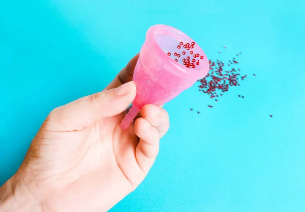 Mão feminina com uma xícara menstrual em um fundo azul — Fotografia de Stock