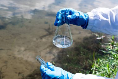 Analiz, nehirden alınan su örneği, göl. Eldivenli bir el test tüpünde su toplar. Ekoloji, çevre kirliliği kavramı