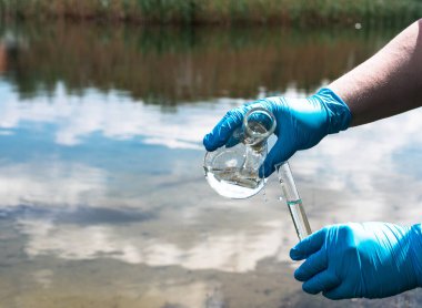 Kirlilik için nehirden gelen suyun analizi. Mavi bir eldivenin içinde bir test tüpü var. Çevre kirliliği, ekoloji kavramı