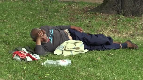 OLOMOUC, CZECH REPUBLIC, MAY 5, 2018: Authentic emotion face homeless man lies relax in park in grass and has a mess around him drunk homeless man in city, the poor man on the brink of society — Stock Video