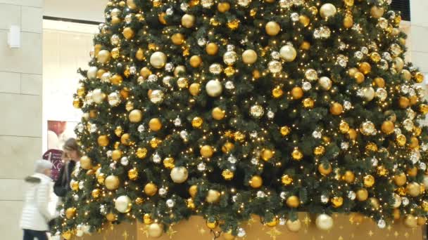 BRNO, ЧЕШСКАЯ РЕСПУБЛИКА, 21 ДЕКАБРЯ 2018: Рождественская елка искусственная пластиковая елка с украшениями и рождественский шар золотые колбы колбы украшения в торговом центре, люди ходят вокруг — стоковое видео