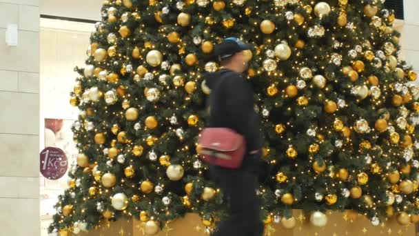 Brno, Tsjechië, 21 december 2018: kerstboom kunstmatige kunststof boom met decoraties en Xmas bal gouden lamp kolven decoraties in het winkelcentrum, mensen rond te lopen — Stockvideo
