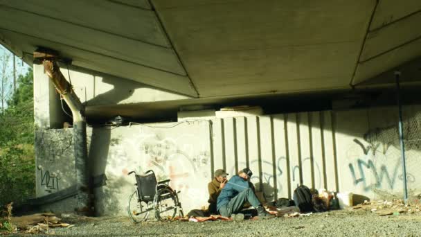 Olomouc, Tschechische Republik, 24. Oktober 2018: Eine Gruppe von Obdachlosen und ein Rollstuhlfahrer ohne Beine sitzen unter einer Brücke, wo sie schlafen, Europa — Stockvideo