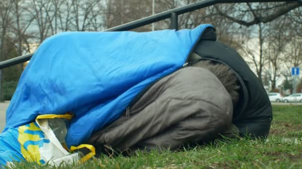 OLOMOUC, REPÚBLICA CHECA, JANEIRO 2, 2019: Sem-teto dormindo e acorda do sono em saco de dormir na rua perto de lojas de departamento, andando pessoas vida parque da cidade, emoção autêntica — Vídeo de Stock