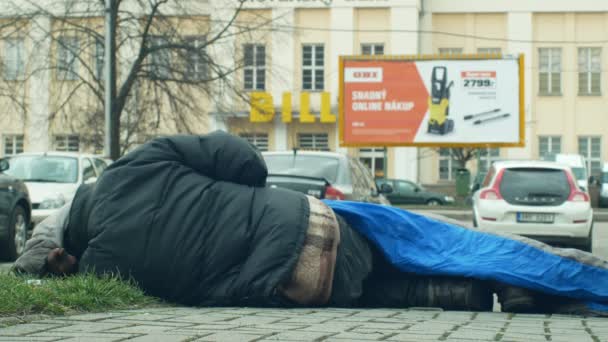 OLOMOUC, REPUBBLICA CECA, 2 GENNAIO 2019: Autentico senzatetto che dorme e dorme nel sacco a pelo per strada vicino ai grandi magazzini negozio, cammina persone vita città vento — Video Stock
