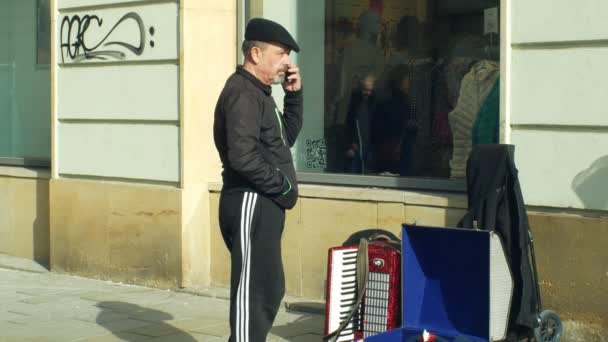 オロモウツ、チェコ共和国、2019年1月29日:高価な携帯電話で偽の乞食の電話、カップにお金を乞う市内のジプシーの男、本物の音楽アコーディオンハーモニカを演奏 — ストック動画