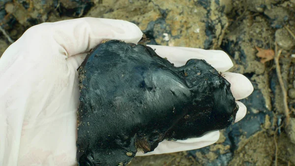 Zehirli katran asfalt kimyasal eldiven el detay. Eski damperli atıklar, kimyasallar ve yağ ile kirlenmiş toprak ve sudan doğa etkileri, siyah bitüm rafine sentetik malzeme yakın çekim