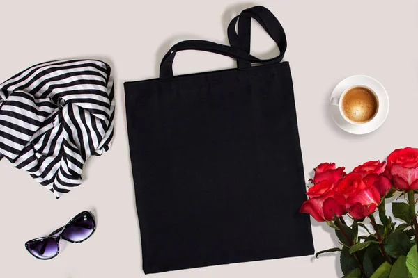 Black blank cotton eco tote bag with red roses, glasses, scarf and a cup of coffee, styled design mockup