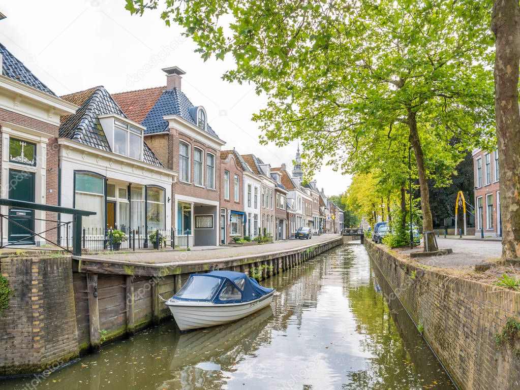 Canal with trees, boat and historic houses in old town of Bolsward, Friesland, Netherlands