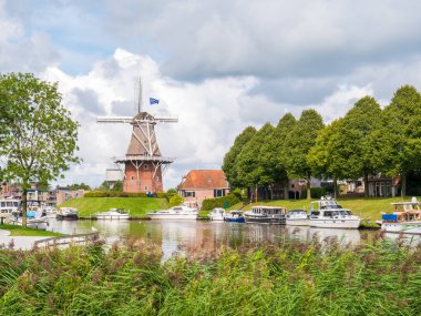 Motorboats on canal and windmill on fortifications of historic fortified town of Dokkum, Friesland, Netherlands clipart