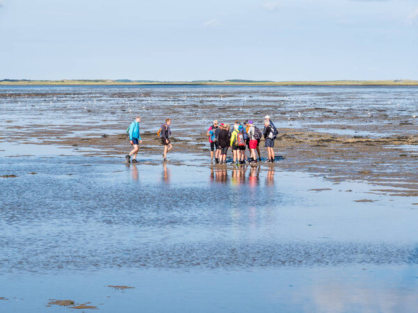 AMELAND, NETHERLANDS - AUG 27, 2017: Group of people mud flat hiking on Wadden Sea at low tide from Friesland to West Frisian island Ameland, Netherlands