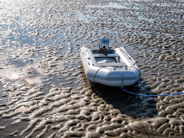 Inflatable rubber boat with outboard motor on sand flat of Wadden Sea at low tide, Netherlands