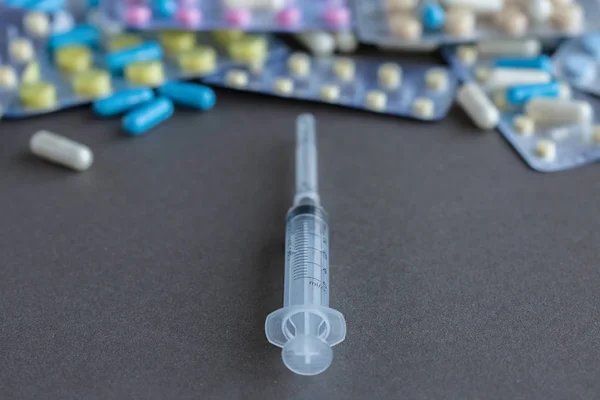 Syringe with assorted pharmaceutical packaging of tablets and pills on gray background