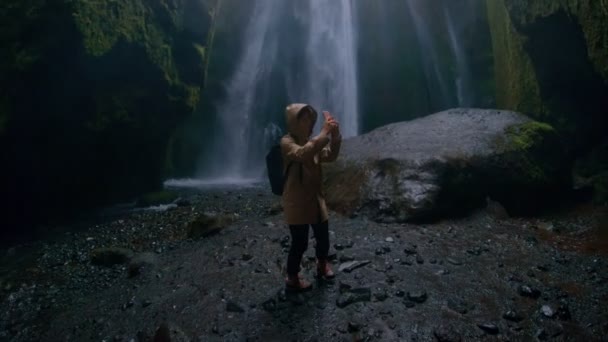 Mladá cestovní blogger v epické jeskyně s vodopádem — Stock video