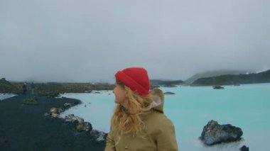 Genç maceracı kadın fotoğrafçı kahverengi yağmur ceket ve kırmızı bere ile Doğal kaplıcalar, mavi silikon dioksit su epik peyzaj yürür. Blogger hedef, seyahat