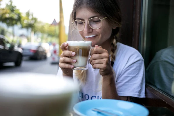 Cute pretty young woman drinks coffee milk foam — Stock Photo, Image