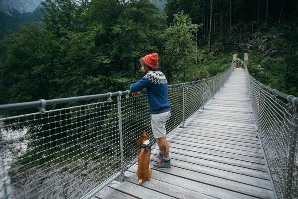 ฮิปสเตอร์นักปีนเขาชายและสุนัขบนสะพานแขวน ภาพถ่ายสต็อกที่ปลอดค่าลิขสิทธิ์