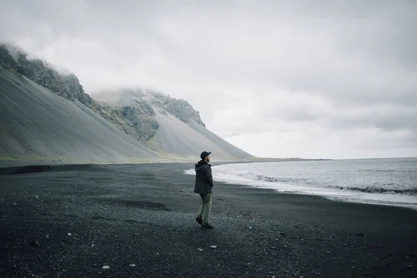 Lonely man walks on grey black volcanic sand beach — Stock Photo, Image