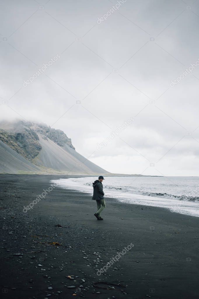 Lonely man walks on grey black volcanic sand beach