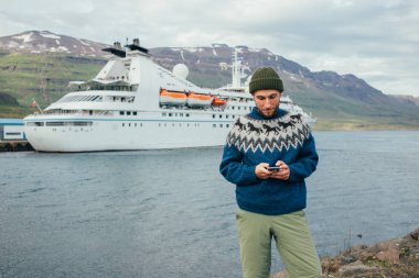 Hipster millennial man texts in fjord port clipart
