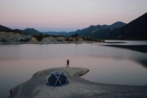 Lonely man stands next to camping tent with dog