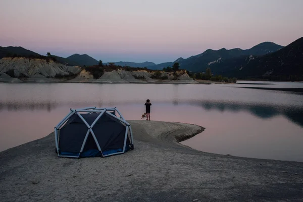 Homem solitário fica ao lado de barraca de acampamento com cão — Fotografia de Stock