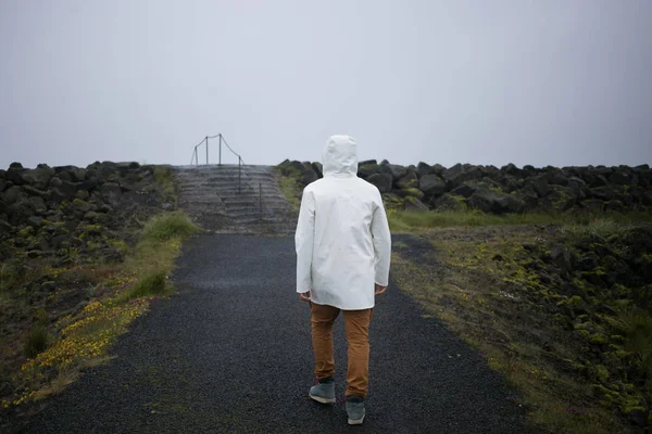 白いレインコートで観光アイスランドの海岸の上を歩く — ストック写真