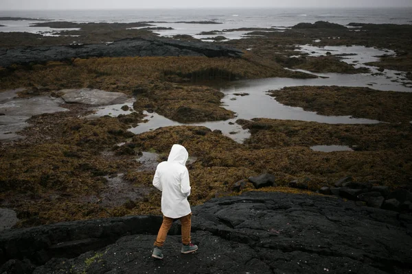 Tourist in white raincoat walks on iceland shore — Stock Photo, Image