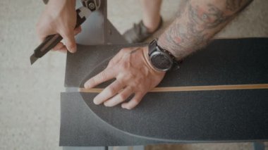 Düz Kollarında dövmeler olan adam atış yukarıdan, bin yıllık yeni nesil aktif spor sevgilisi ya da kaykaycı eski longboard regrip gösterilmiştir. Aşırı kavrama bant kesici ile keser