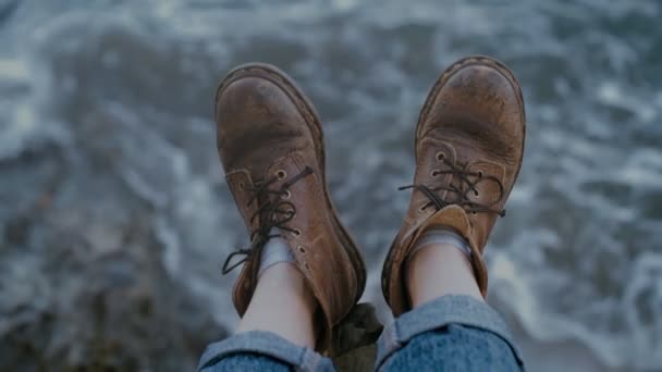 Old hiking boots at edge of cliff over water — Stock Video