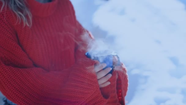 Femme en pull rouge tient tasse de café bleu à l'extérieur — Video