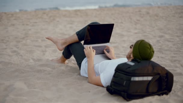 Millennial nómada trabaja en el ordenador portátil en la playa — Vídeo de stock