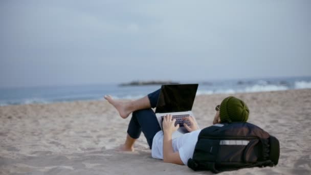 Milenyal göçük plajda laptop üzerinde çalışıyor — Stok video