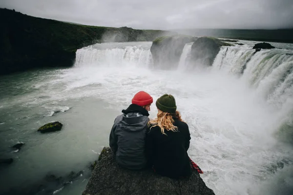 Casal senta-se na borda do penhasco em enorme cachoeira — Fotografia de Stock